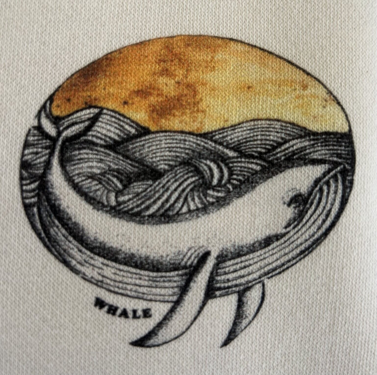 Detalle real del estampado Ballena Art con ballena, olas y sol dorado